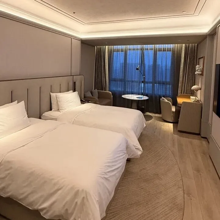 A hotel twin room with two made-up beds, a desk and a curtained city view