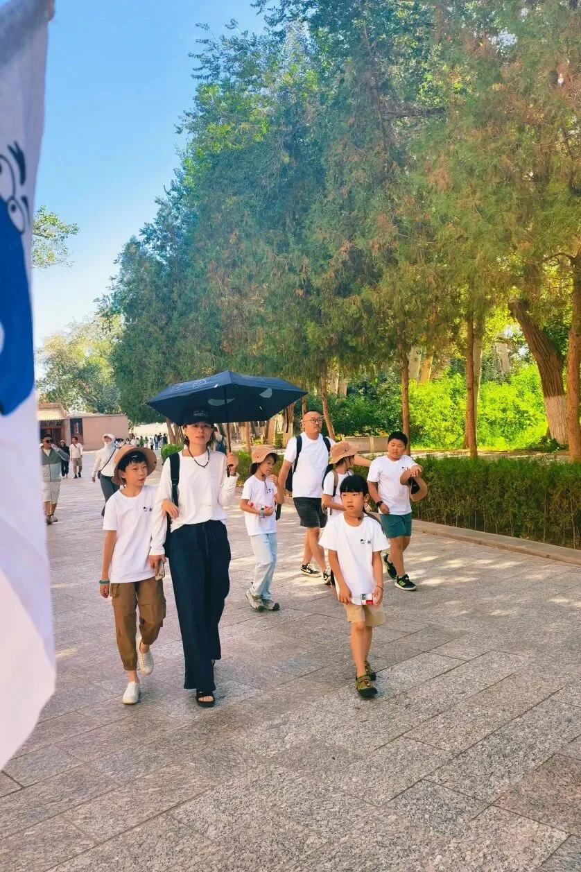 Group walking a tree-lined stone path behind a guide with a black umbrella