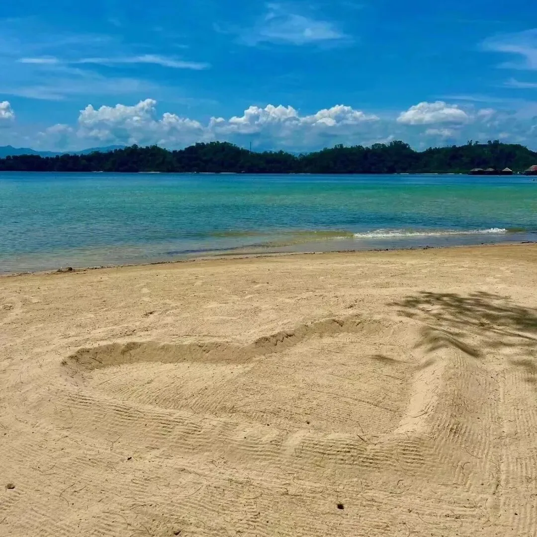 An empty sandy beach curving into turquoise water, with forested islands on the horizon.