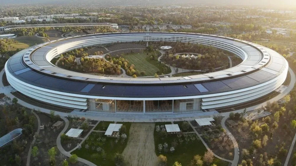 A ring-shaped, solar-panelled corporate campus set among trees in Silicon Valley, seen from the air.