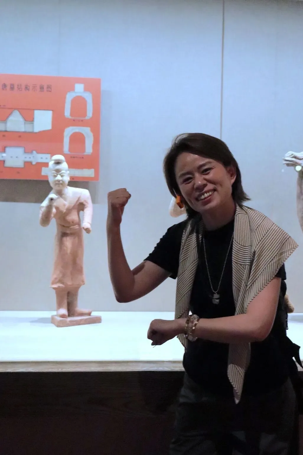 Guide beside a pale standing figurine on a plinth, a cave-structure diagram behind