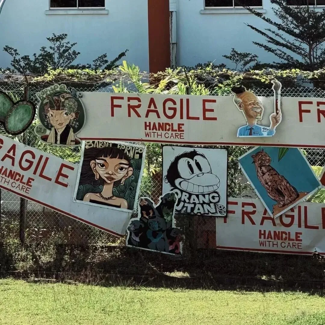 Street-art fence reading Fragile, Handle With Care, hung with painted portraits, an orangutan cartoon and a clouded leopard.
