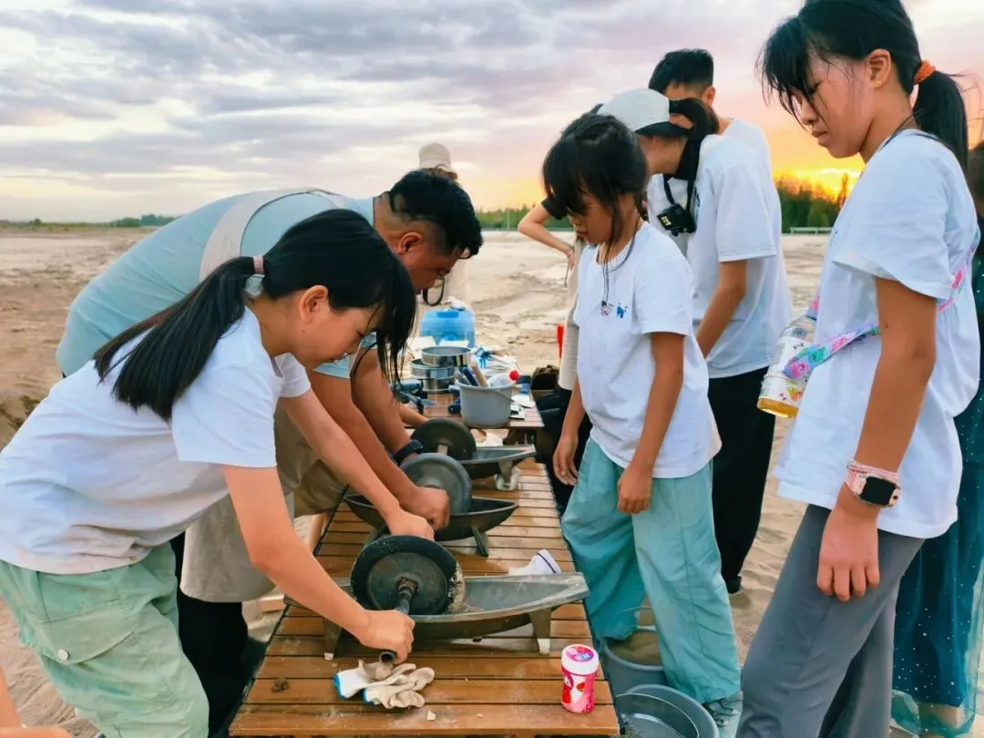 Children and instructors working stone grinding wheels on a trestle table at sunset