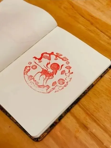 Open notebook with a single round red seal impression of a figure among clouds