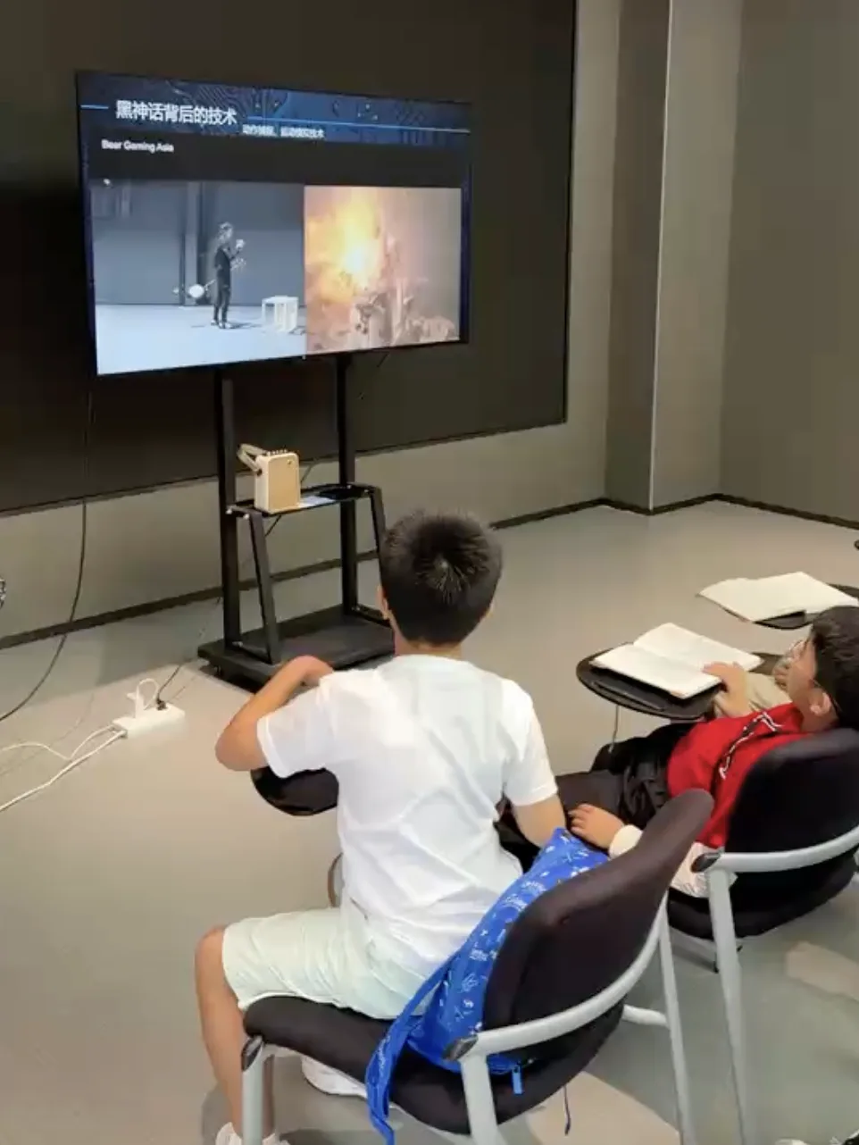 Two boys watch a screen presentation on the technology behind the game Black Myth