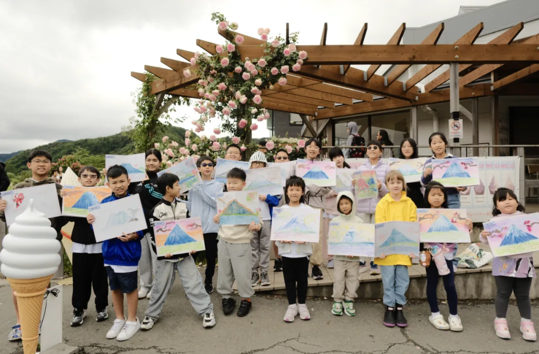 Children holding up their watercolour paintings of Mount Fuji beneath a rose-covered pergola
