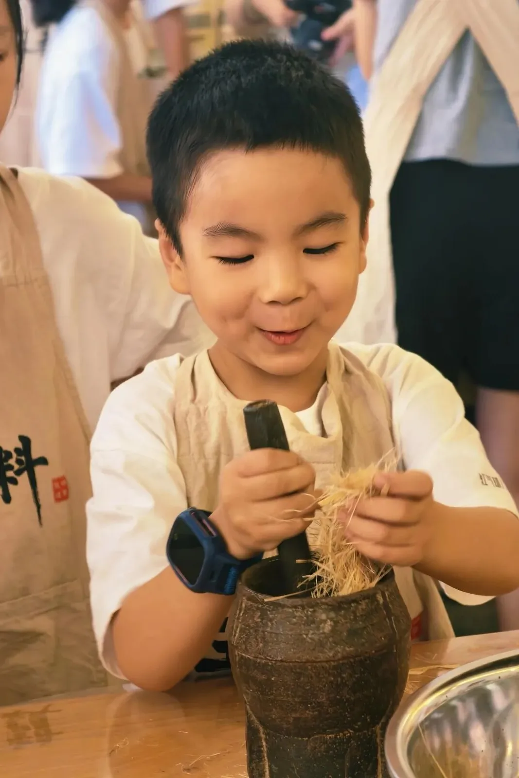 Boy in a linen apron pounding pale hemp fibre in a stone mortar with a pestle