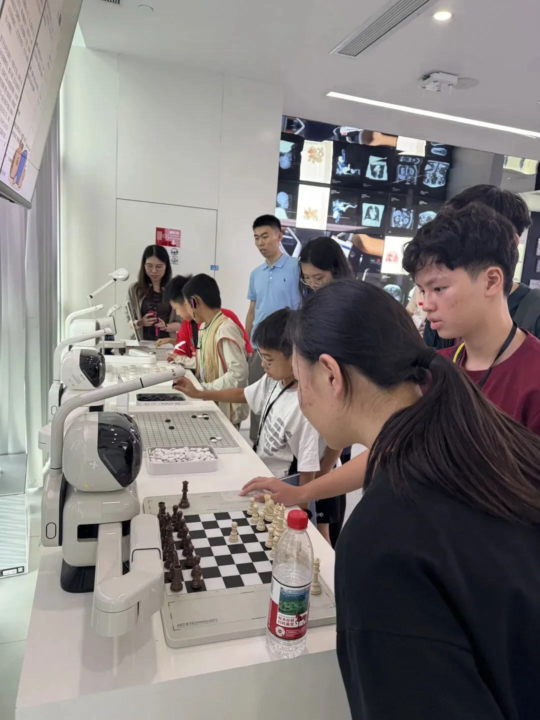 Visitors play chess and Go against white robotic arms at a row of AI demonstration stations
