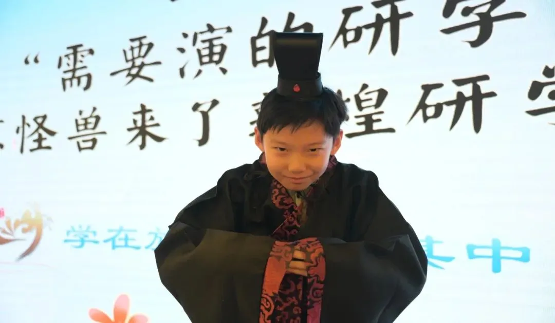 Boy in a black scholar's robe and cap on stage at the opening ceremony