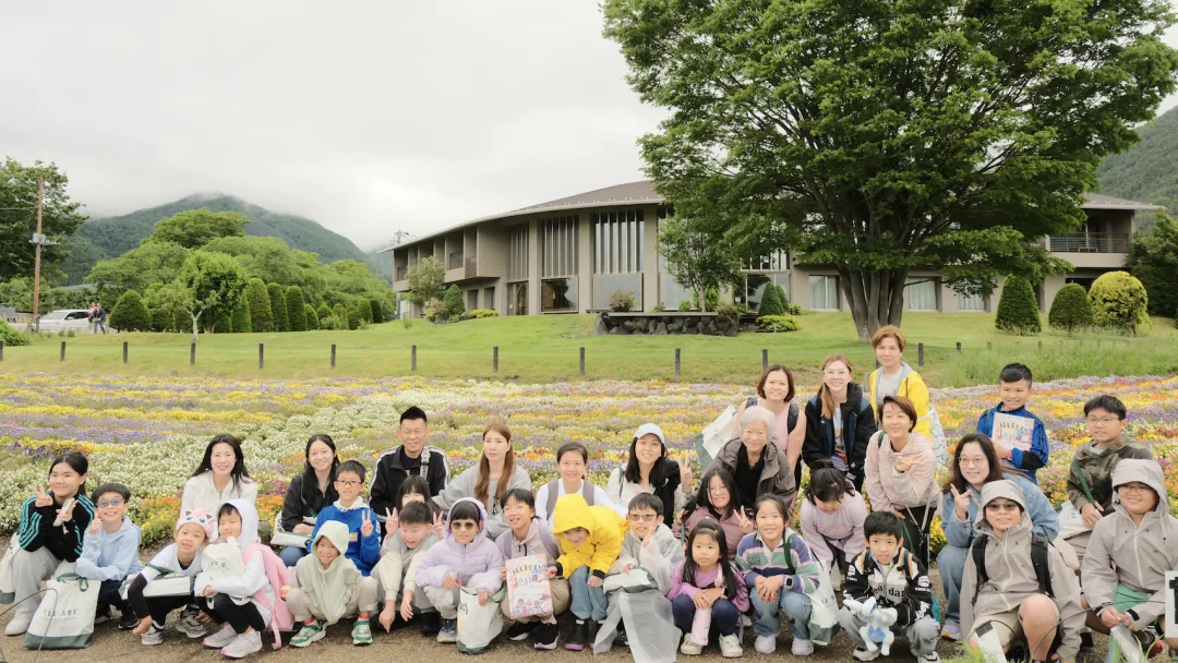 The whole group posing in front of a flower field and a lodge below misty hills