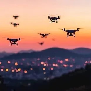Five quadcopter drones hovering above a city skyline at sunset.