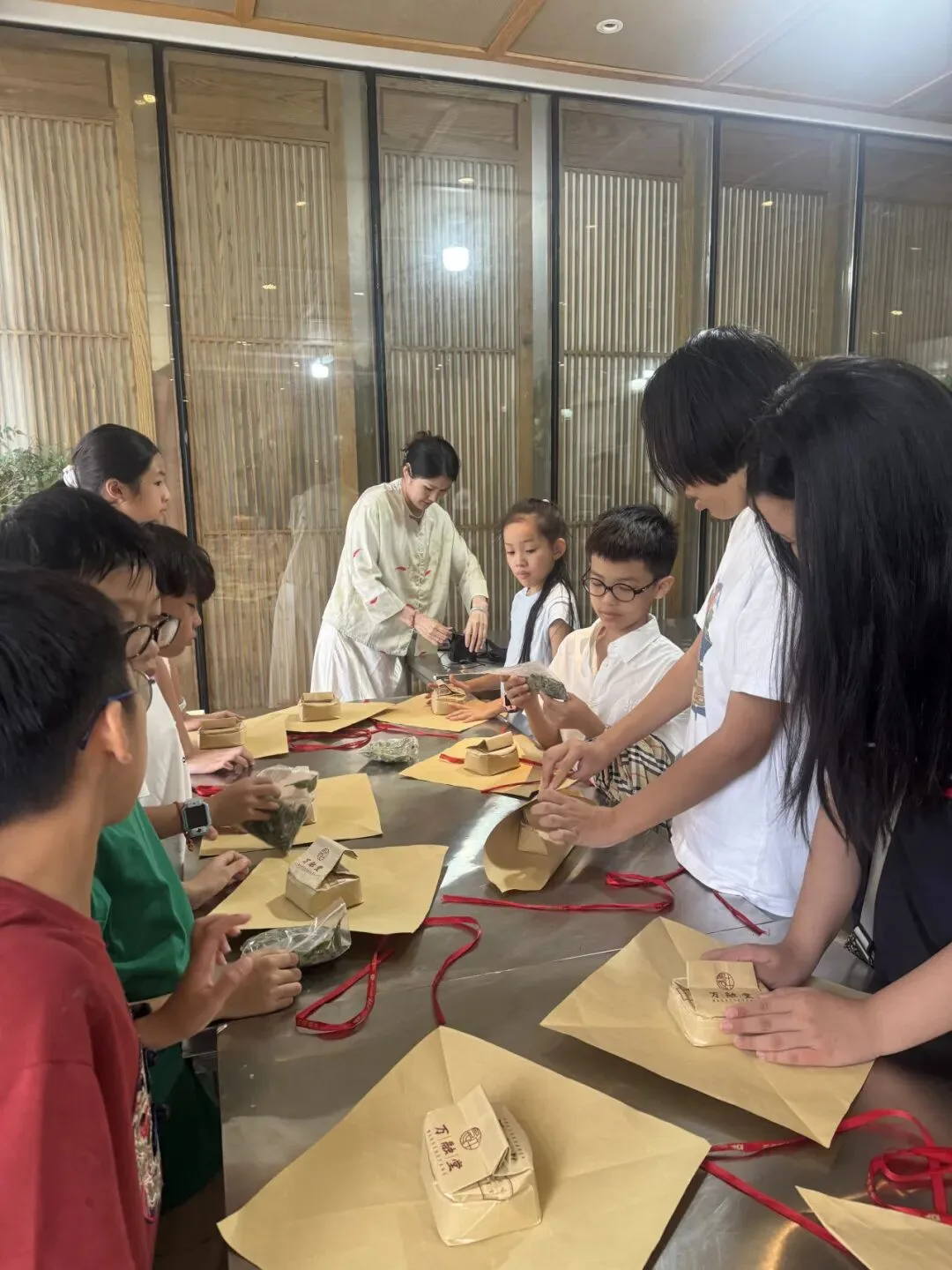 Children pack their tea into kraft-paper parcels tied with red cord, guided by an instructor