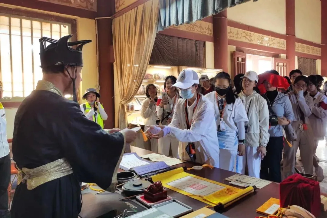 Costumed official in a winged cap handing a paper pass across a desk of seals and scrolls
