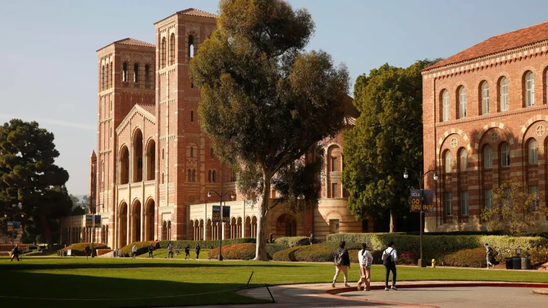 Students walking past UCLA's twin-towered brick hall under Go Bruins banners.