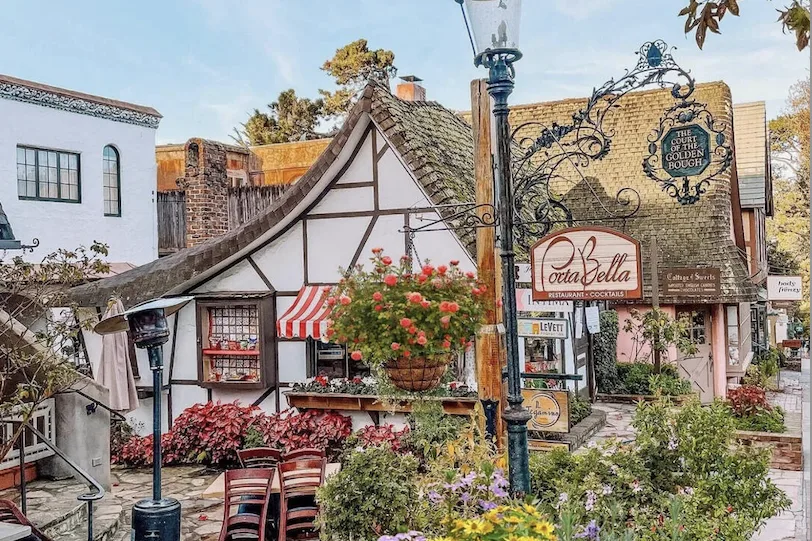 A storybook cottage restaurant in Carmel-by-the-Sea with hanging flower baskets and painted signs.