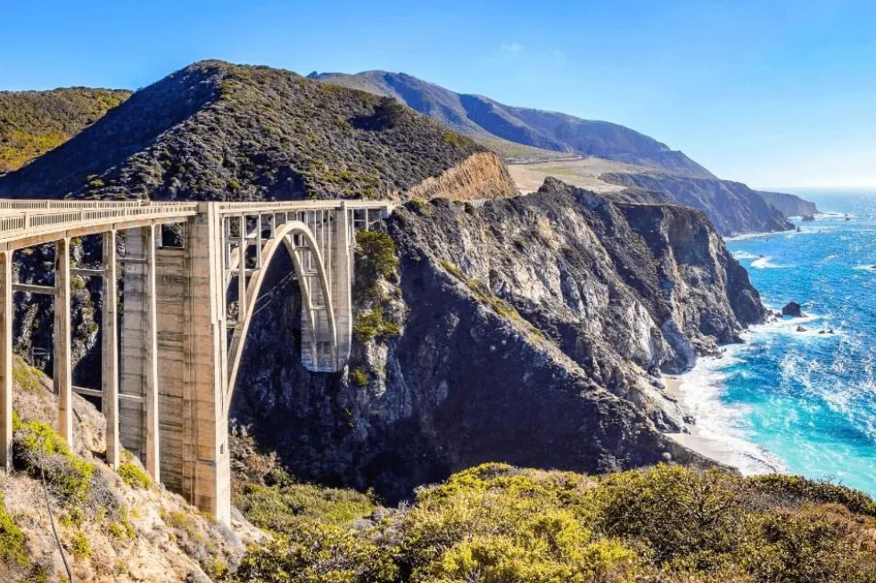 An arched concrete bridge carrying Highway 1 across a canyon above the Pacific coast.