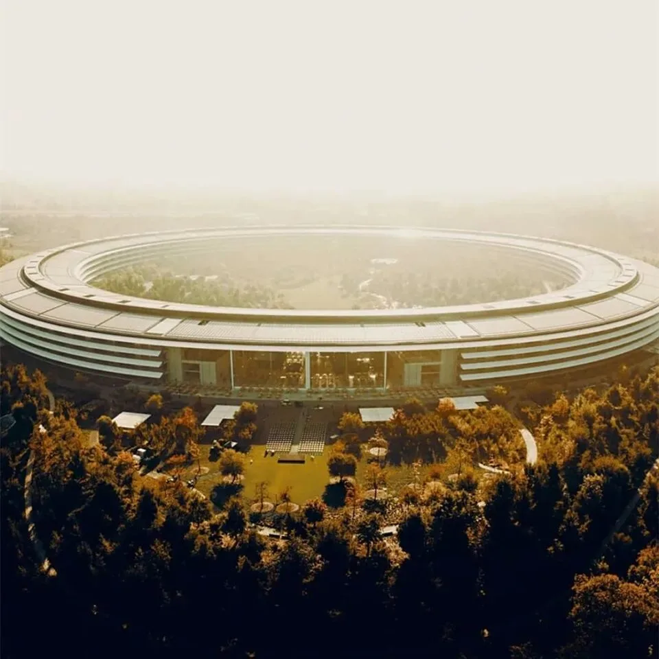 A ring-shaped corporate campus ringed by trees, photographed from the air in golden haze.