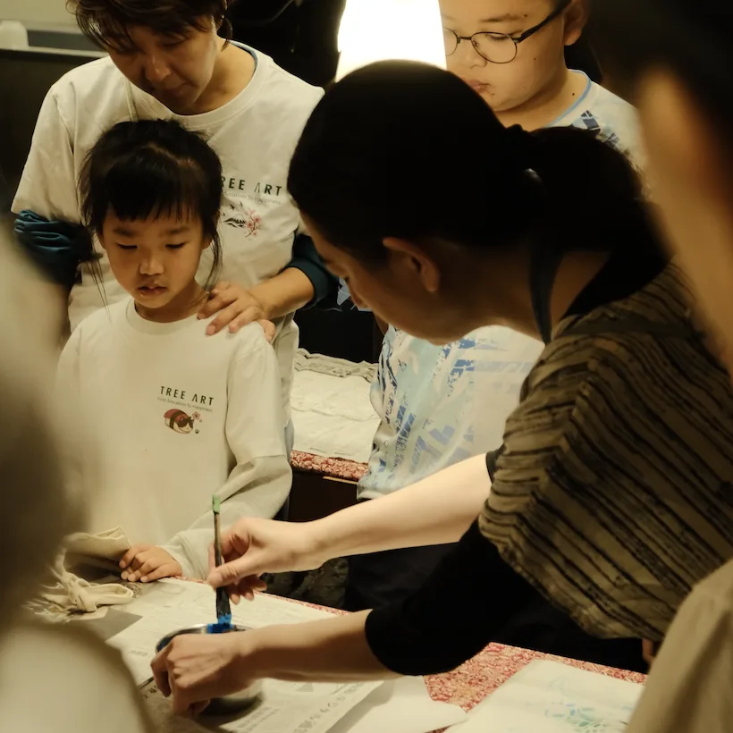 An instructor demonstrating brush dyeing while a girl in a TREE ART shirt watches closely