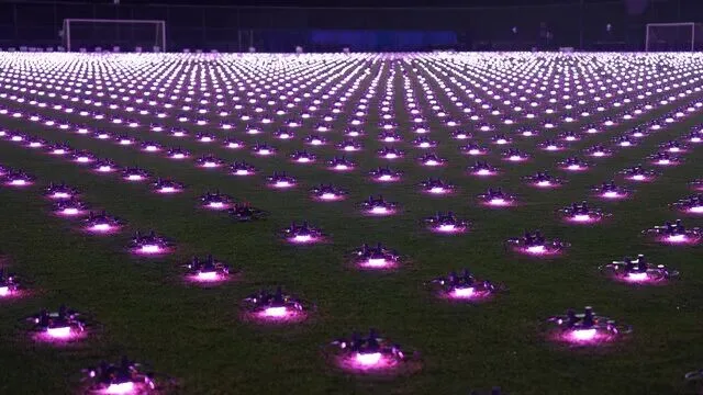夜间球场上密集排列的无人机方阵,粉紫色灯光连成一片。