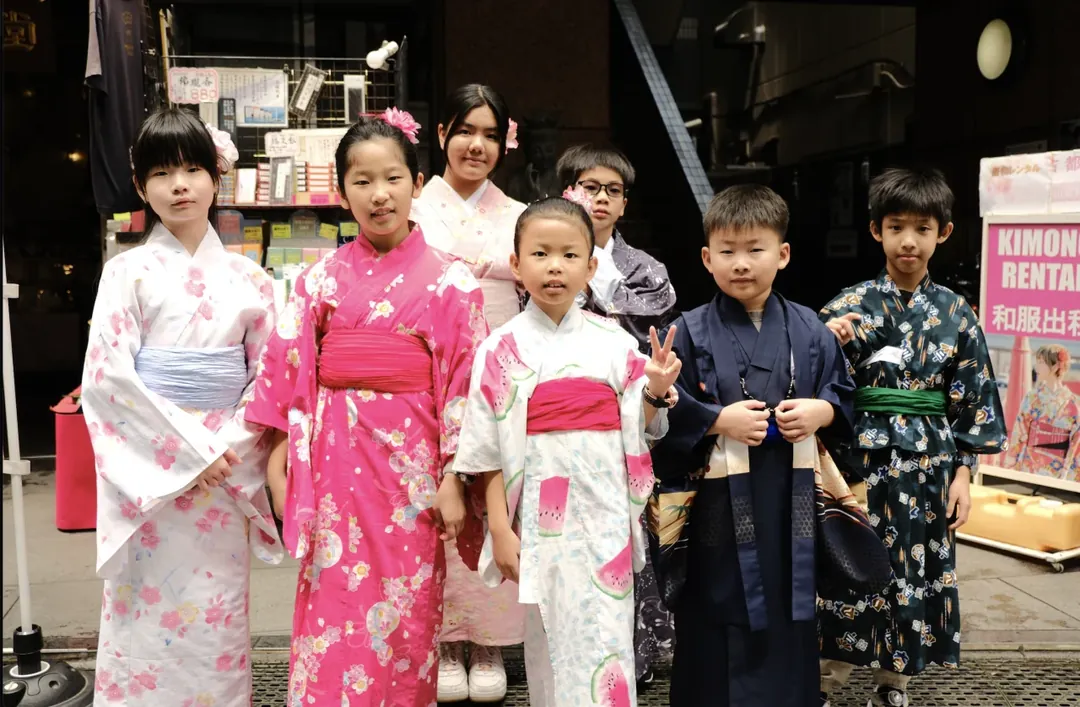 Seven children in summer kimono outside a kimono rental shop